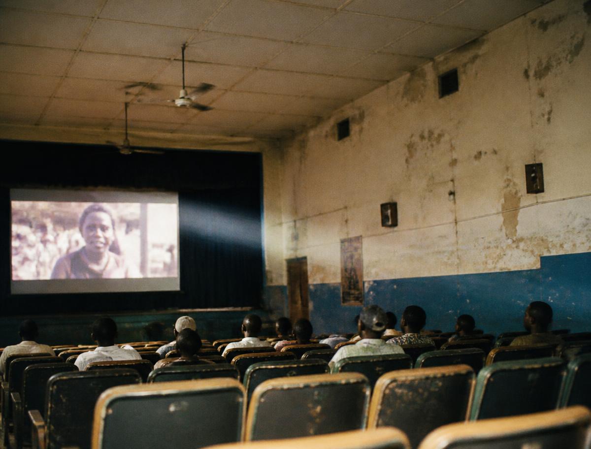 Spectateurs dans une salle de cinéma africaine éclairée par le faisceau du projecteur